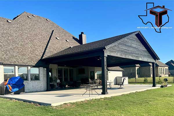 Residential backyard with a patio cover installed by Trutex made of black wood and a black shingle roof