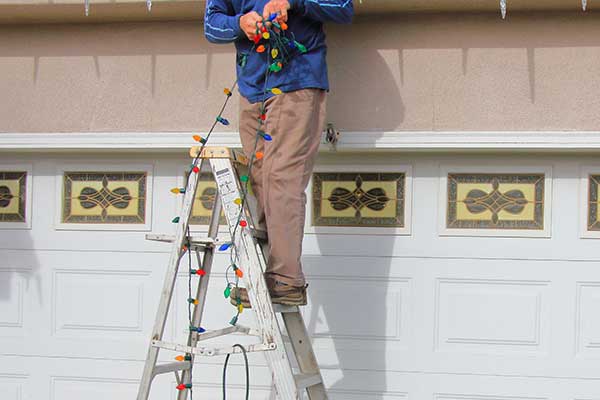 Worker on a ladder about to install large Christmas lights on a home