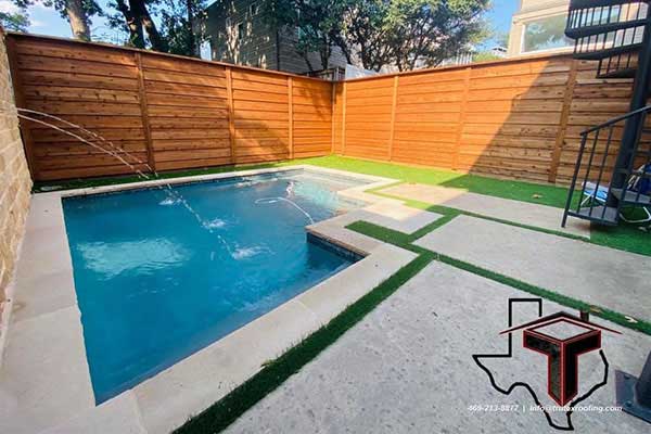 Remodeled swimming pool by Trutex with synthetic grass, concrete panels, and a wooden fence around it all